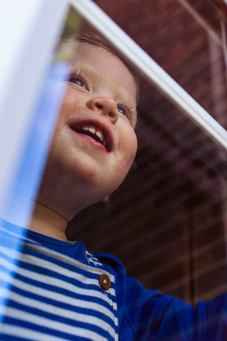 Toddler pressing his face up against a window during a family photo session