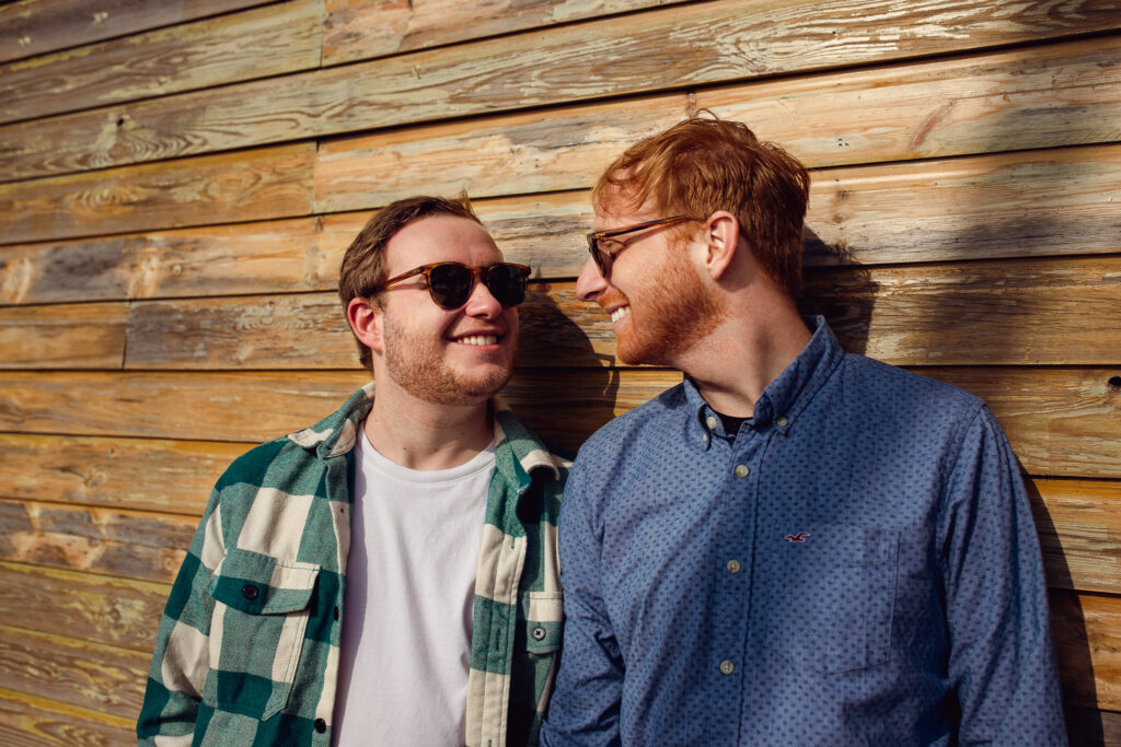 LGBTQ+ couple at their engagement session looking at each other by a wooden decked wall