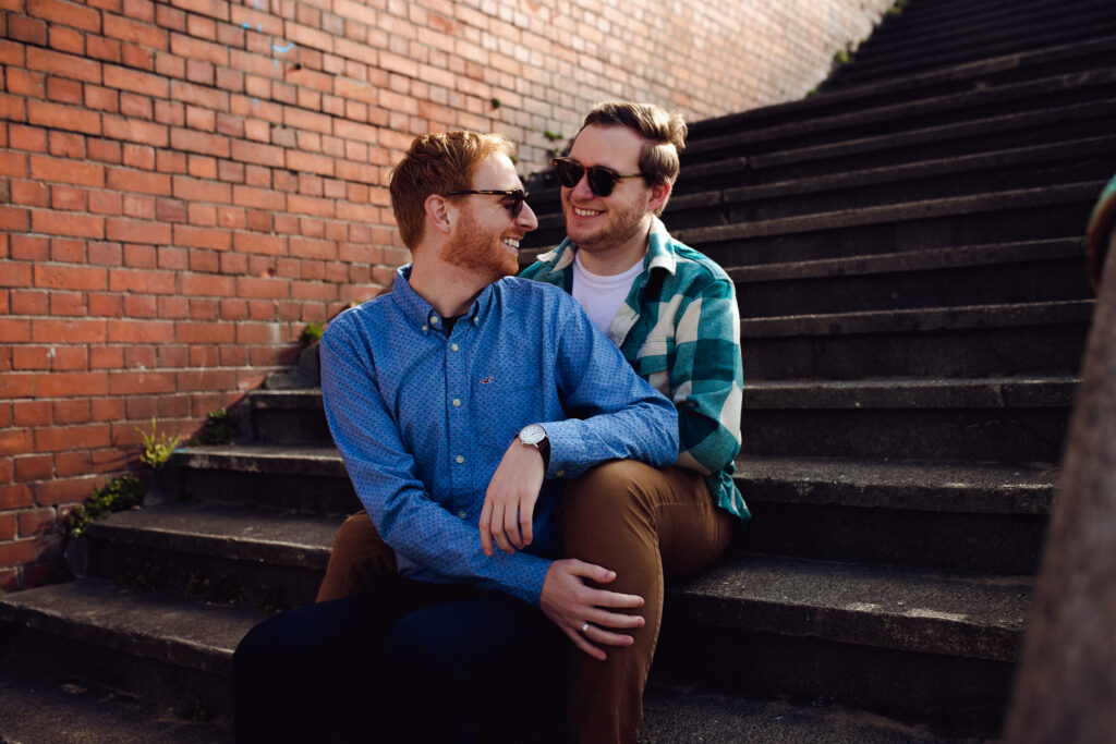 LGBTQ+ couple sitting on the stairs at their engagement session on Brighton Beach