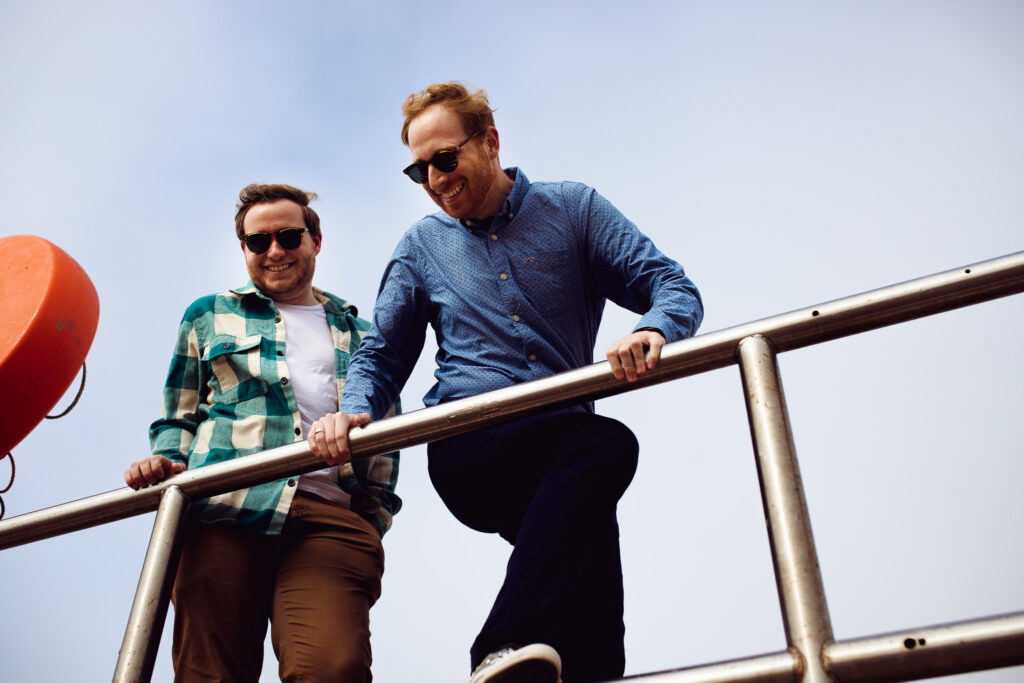 LGBTQ+ couple climb up a fence and laugh during their Brighton engagement session