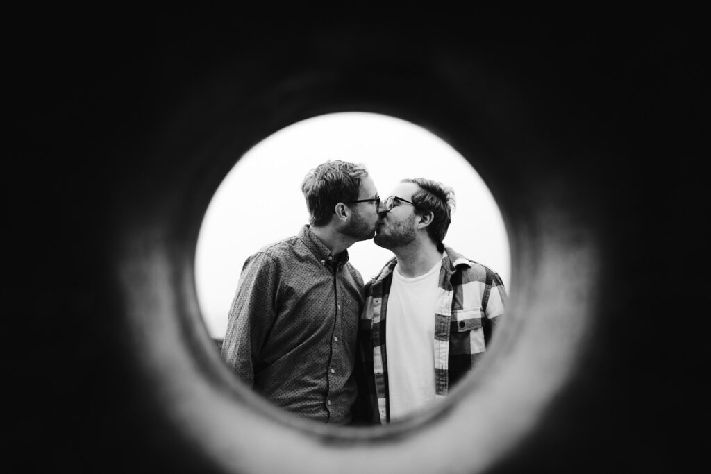 LGBTQ+ couple kissing behind the doughnut statue on Brighton Beach during their engagement session