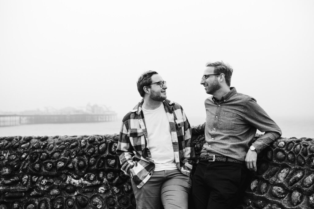 Engagement session of an LGBTQ+ couple looking at each other next to Brighton Pier