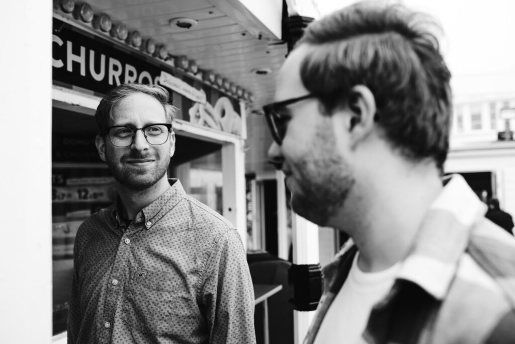 LGBTQ+ couple looking at each other at a churros stand on Brighton pier during their engagement session