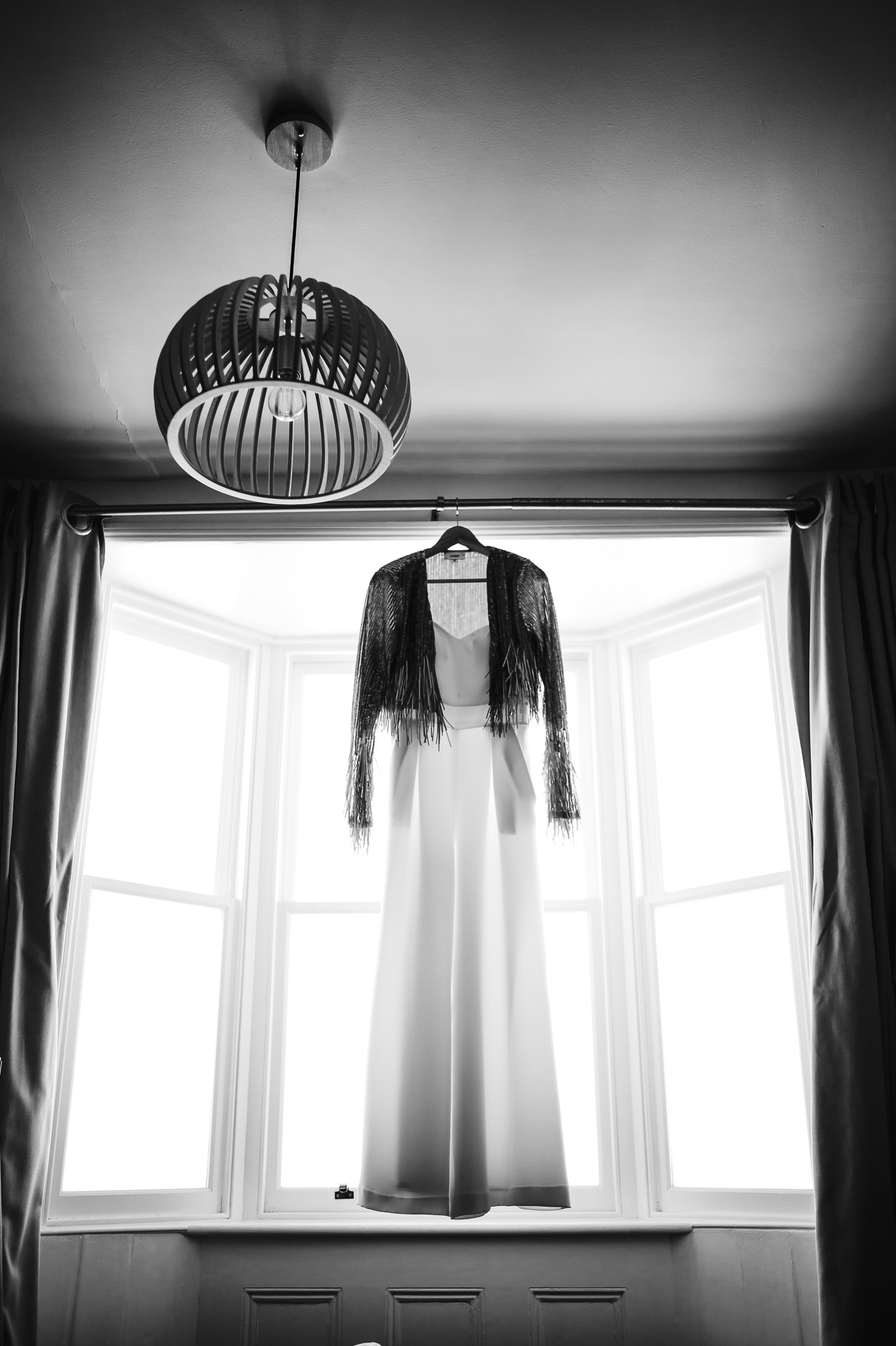 A beautiful wedding suit hangs backlit in a window with a sequin jacket