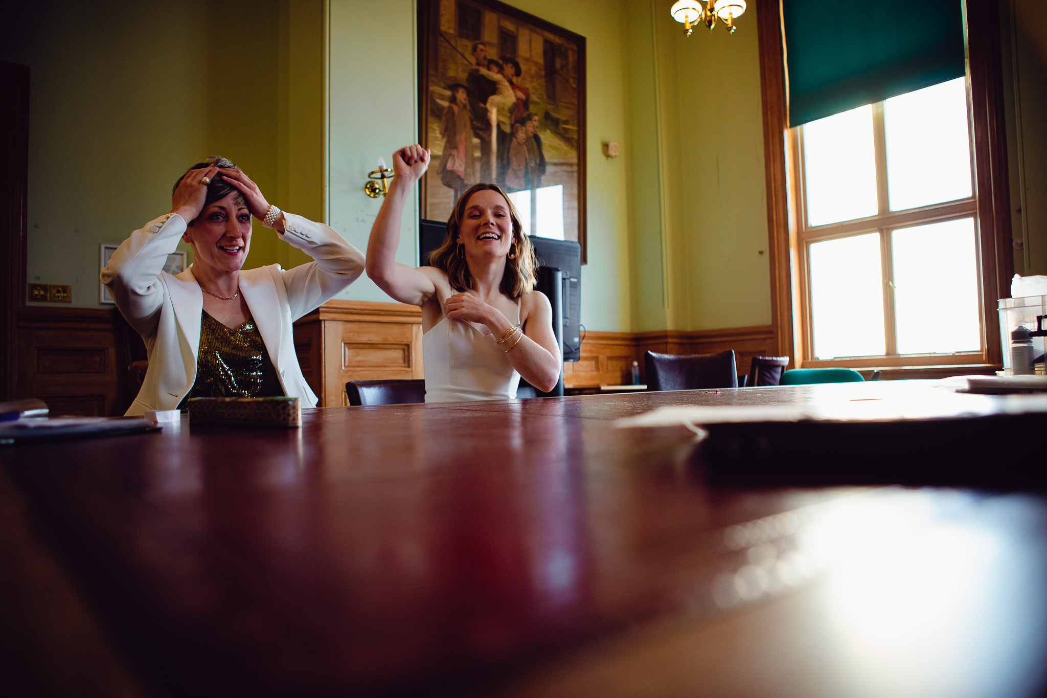 Gemma and Natalie smile as they prepare for their wedding ceremony sitting at a table inside Brighton Town Hall.