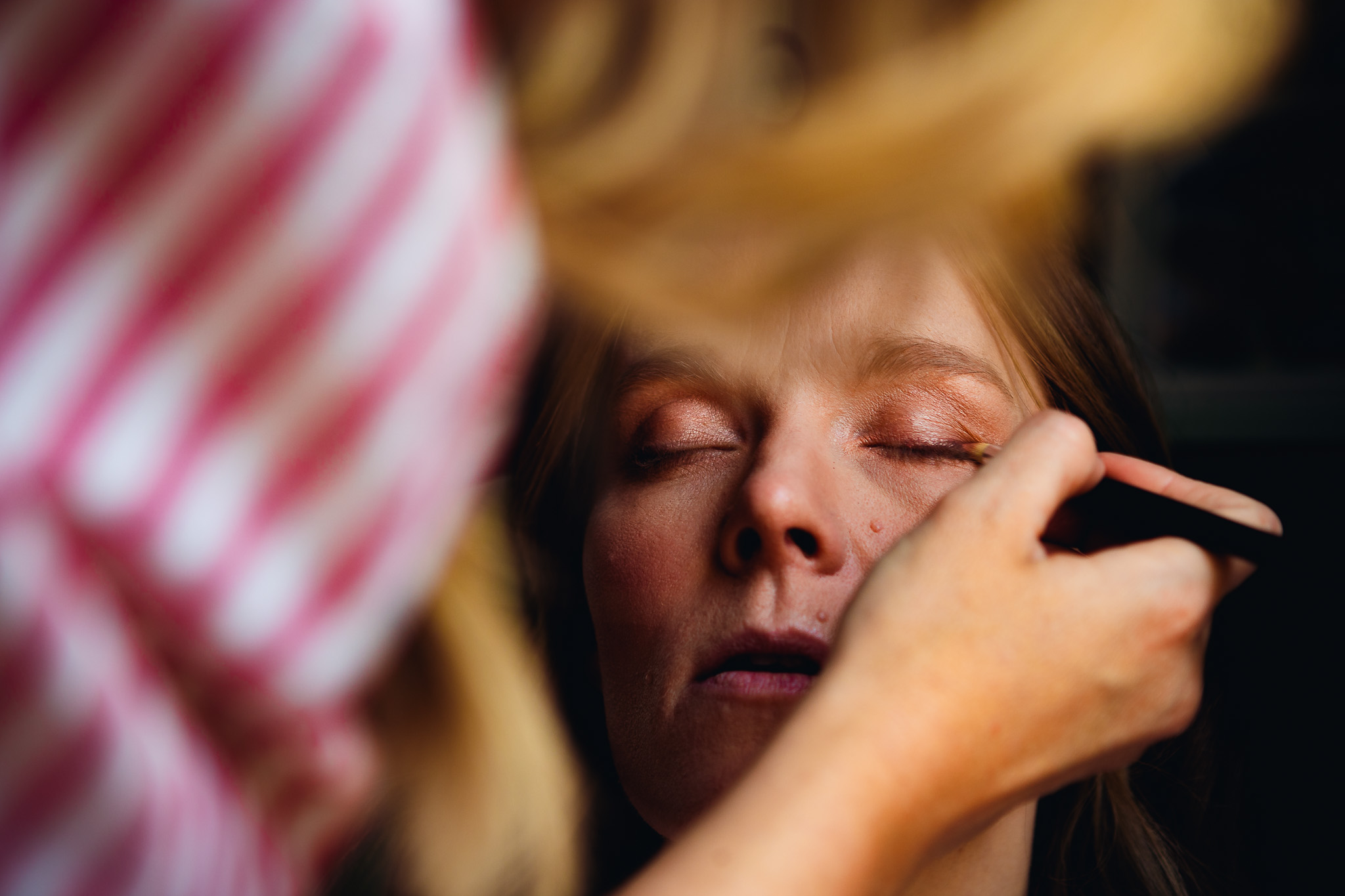 Portrait of the bride as she has her eyeshadow applied by her friend in preparation for her wedding day