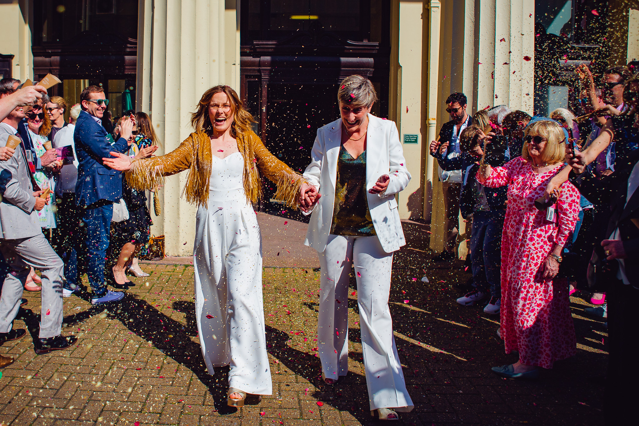 Gemma and Natalie laugh as their guests throw colourful confetti at them outside Brighton Town Hall.