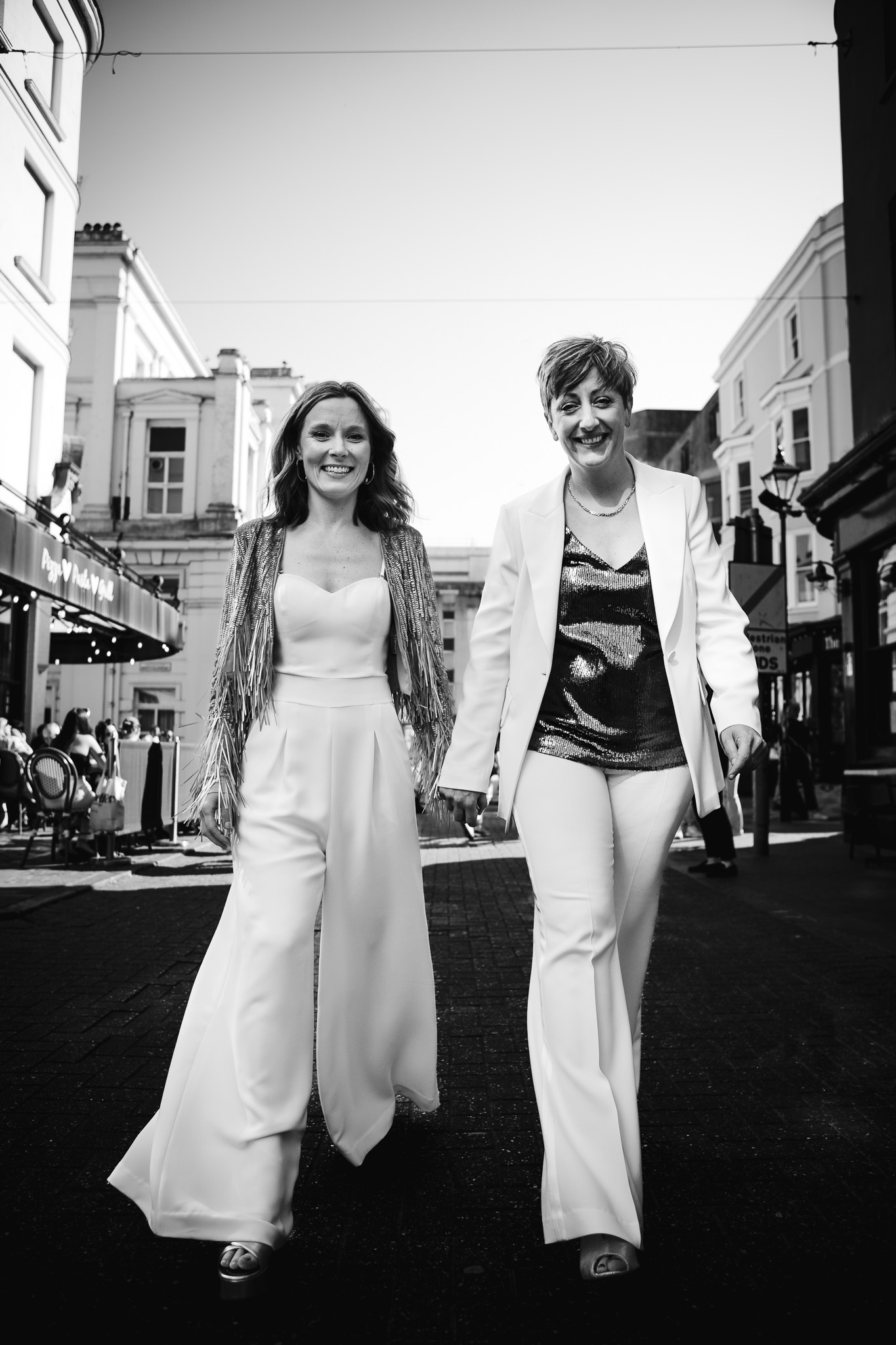 Gemma and Natalie smile as they walk hand in hand together through the Brighton lanes on the way to their wedding reception.