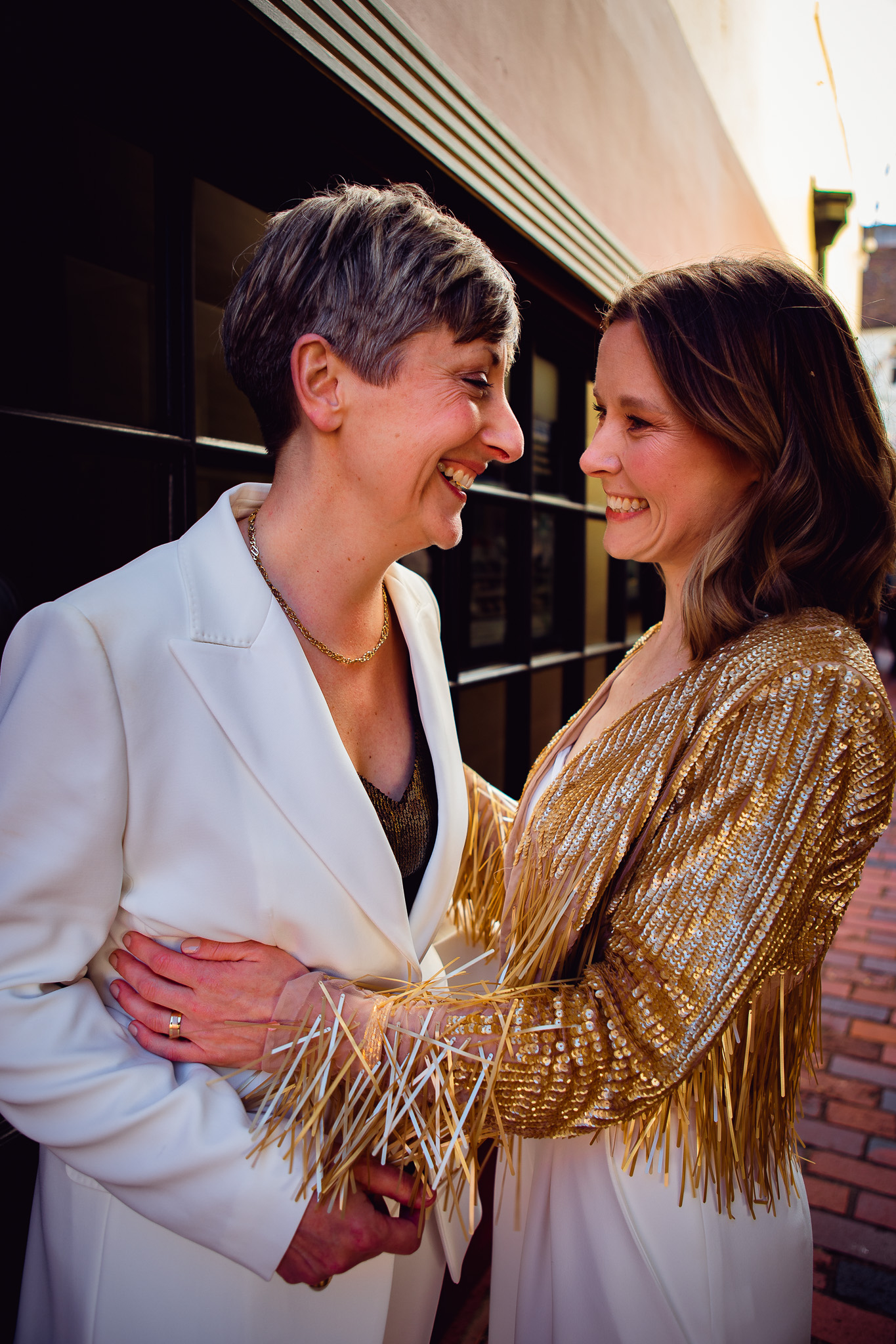 Gemma and Natalie stand smiling at each other as they pose for their couple portraits in the Brighton lanes.