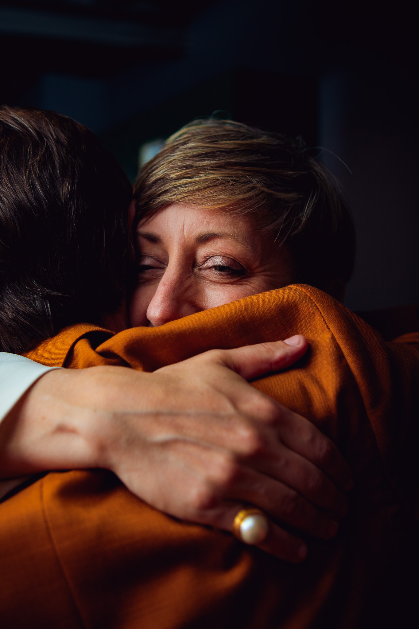 Natalie smiles as she hugs a wedding guest wearing an orange suit.