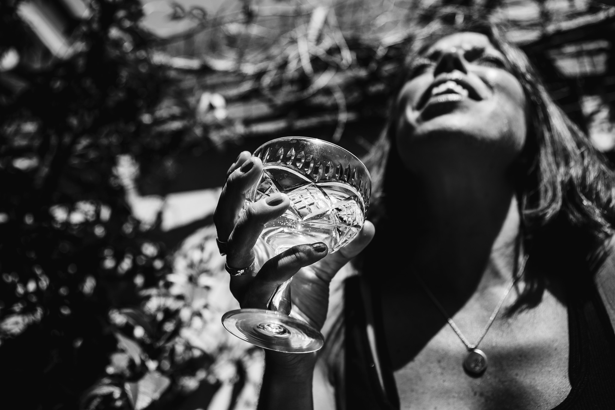 A woman holding a champagne coup in a sunny garden.