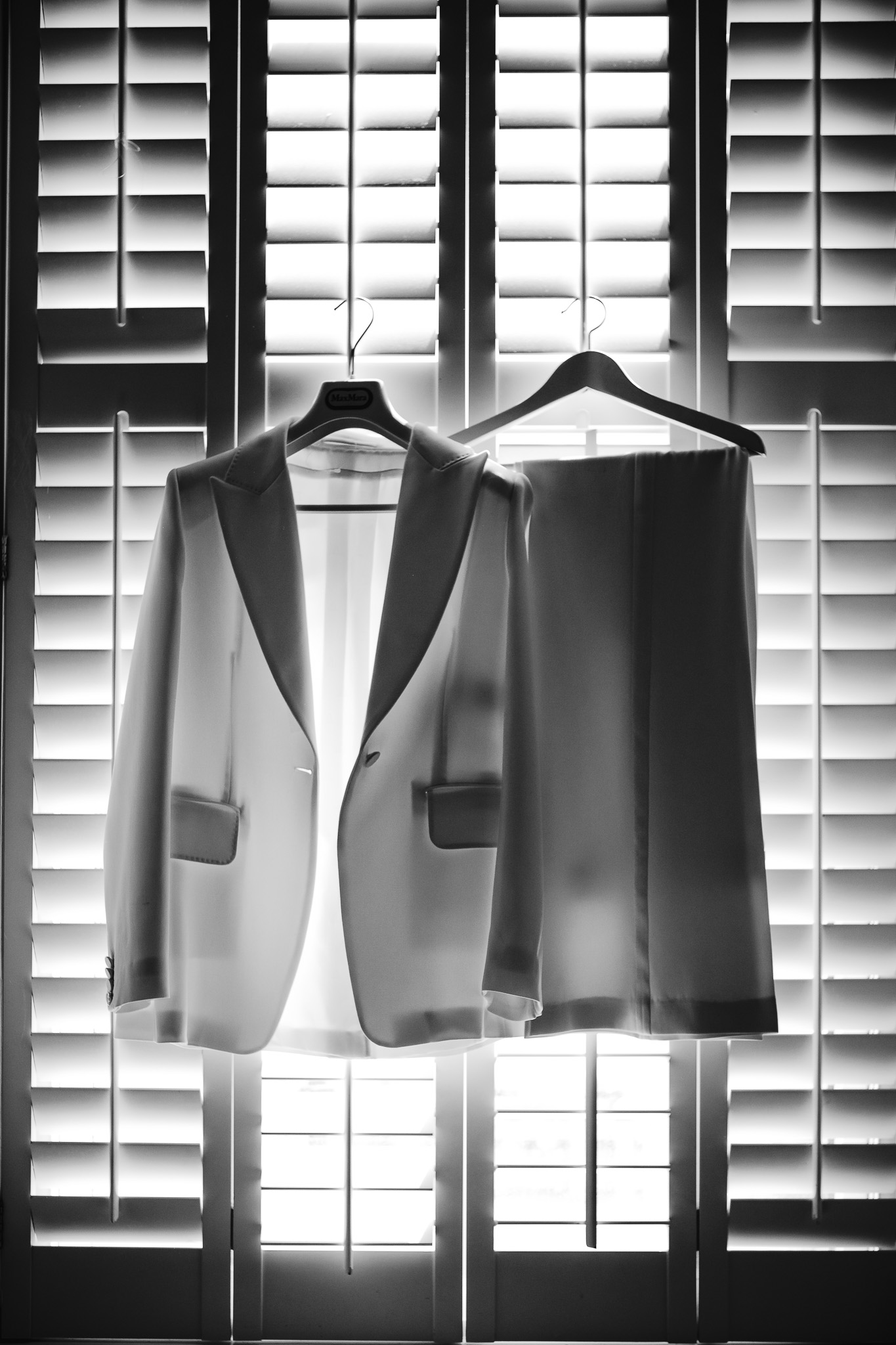 A wedding suit hangs on window shutters whilst backlit from the sun outside.